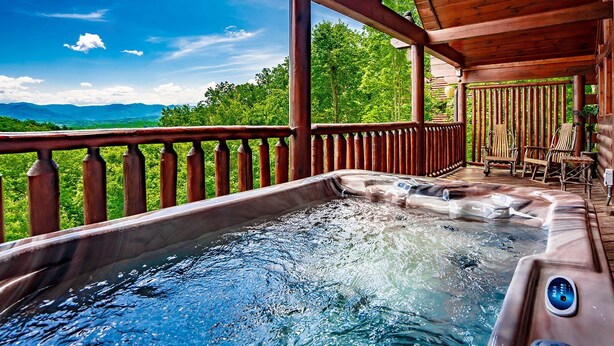 Un bain à remous sur une terrasse en bois, avec vue sur les montagnes et les arbres.
