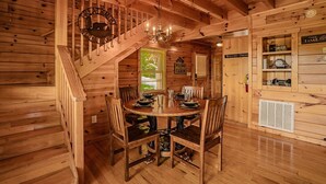 L’intérieur d’une cabane en bois, avec une table à manger dressée pour quatre personnes, un escalier et un panneau indiquant les règles à respecter dans la cabane.