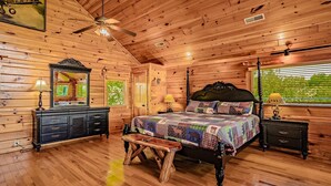Une chambre à coucher dans une cabane en bois, avec un lit à baldaquin, une commode, une coiffeuse et un ventilateur de plafond.