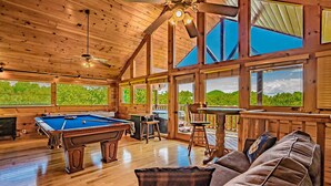 Une pièce spacieuse équipée d’une table de billard, de sièges confortables, de grandes fenêtres et d’un plafond en bois.