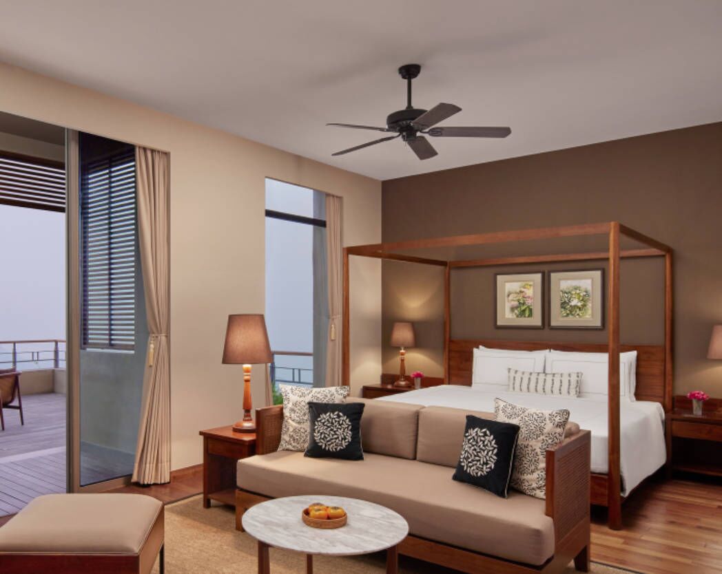 A hotel room with a four-poster bed, a sofa, a round coffee table, and a balcony with a view.