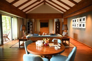 A spacious room with a wooden ceiling, a central seating area, a dining table with chairs, and a television mounted on the wall. - Taj Chia Kutir, Resort & Spa (Kurseong)