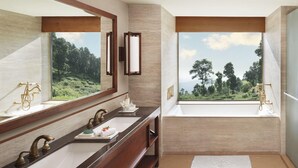 Une salle de bain dotée d’un grand miroir, de deux lavabos, d’une baignoire et d’une fenêtre donnant sur les arbres.