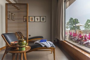 A room with a view of a garden, a wooden chair, a small table with a teapot and a bowl, and framed pictures on the wall. - Taj Chia Kutir, Resort & Spa (Kurseong)