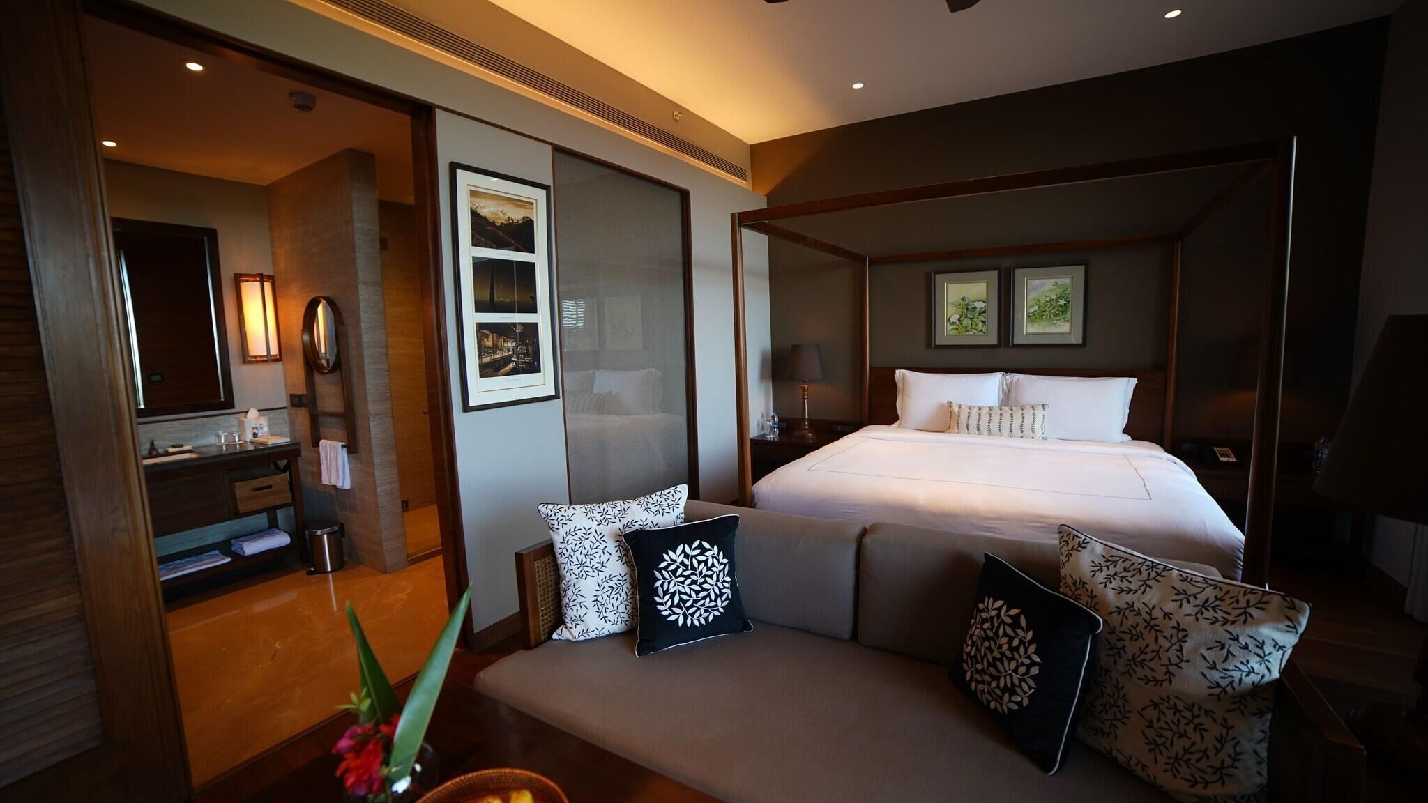 A hotel room with a bed, a bedside table, a mirror, a window, and a wall-mounted picture.