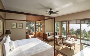 A hotel room with a bed, a desk, a chair, a sofa, and large windows offering a view of the outdoors. - Taj Chia Kutir, Resort & Spa (Kurseong)