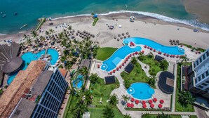 Vista aérea de un complejo turístico con varias piscinas, una playa y una zona frente al mar.