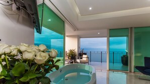 Un baño moderno con bañera, un balcón con vistas y un jarrón con rosas blancas.