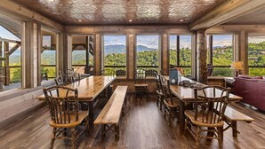 Un comedor rústico con mesas y sillas de madera, ventanas amplias con vistas a la montaña y techo de madera.
