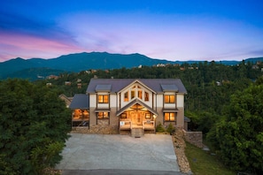 A two-story house with a stone foundation, a front porch, and a driveway. - Splash 'N Heavenly Views – Indoor Pool, Theater & Mountain Views (Gatlinburg)