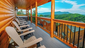 Eine Holzdielen-Terrasse mit Adirondack-Stühlen, einem Geländer und Blick auf grüne Berge.