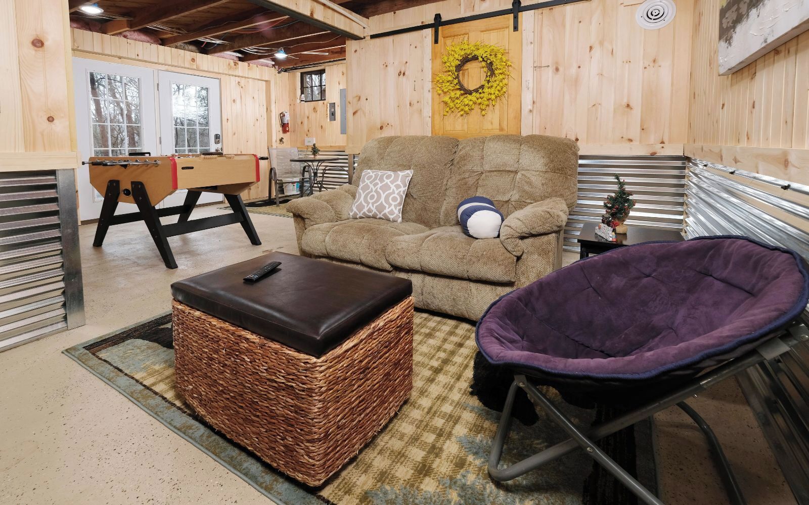 A cozy room with a brown sofa, a purple pet bed, a wicker ottoman, and a metal-framed chair.