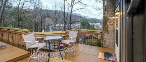 A wooden deck with outdoor furniture, a stone wall, and a view of trees and hills.