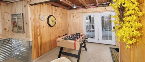 A cozy indoor space with wooden walls, a foosball table, a clock, and a window with a view.