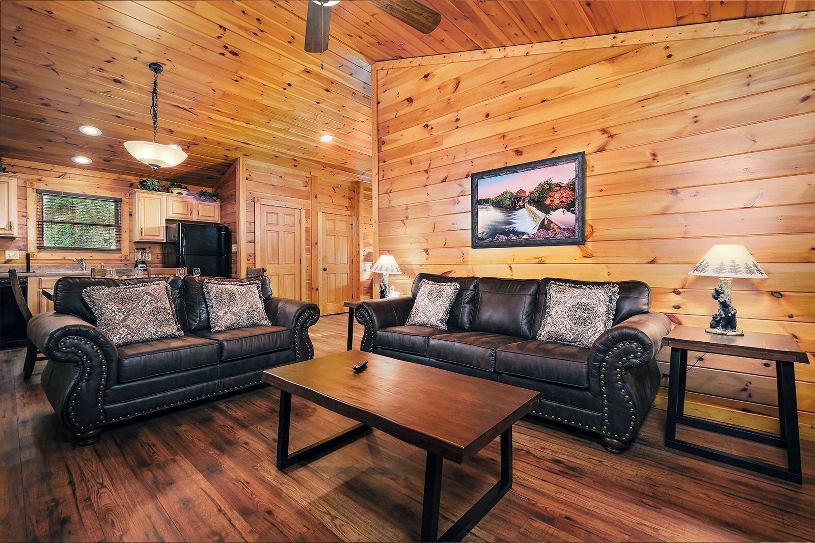 A cozy cabin interior with two leather sofas, a wooden coffee table, and a dining table.