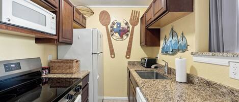 A kitchen with a microwave, stove, refrigerator, and granite countertops.