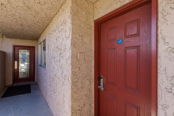 A corridor with a red door marked '105', a door with a glass panel, and a wall with peeling paint.