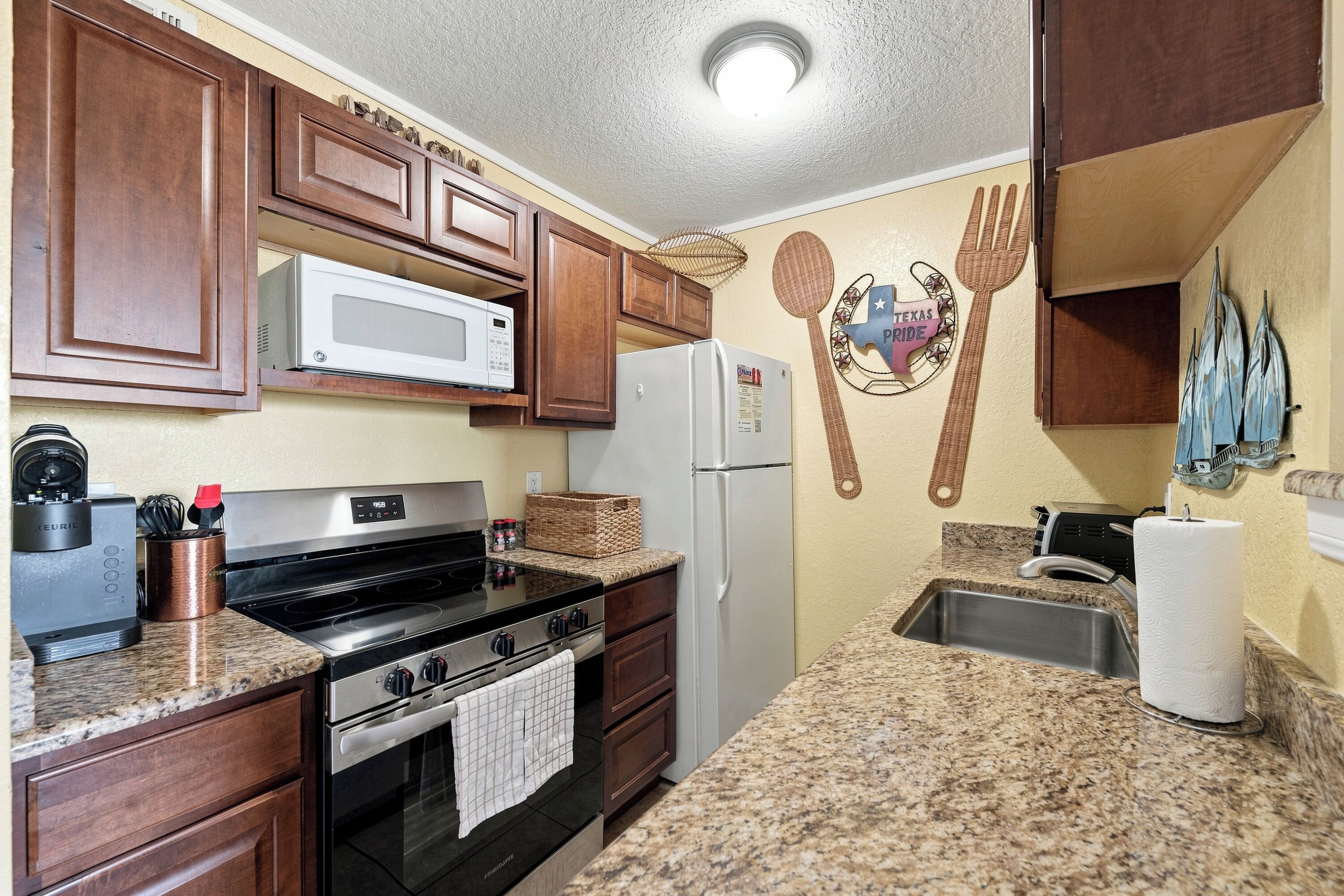A kitchen with wooden cabinets, a microwave, a refrigerator, a stove, and a sink.