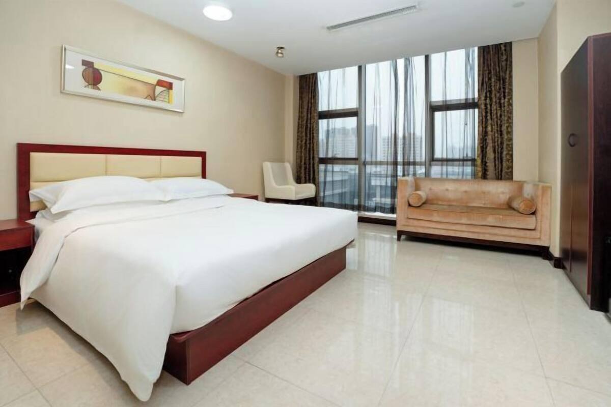 A hotel room with a large bed, a sofa, a chair, and a window with a view.