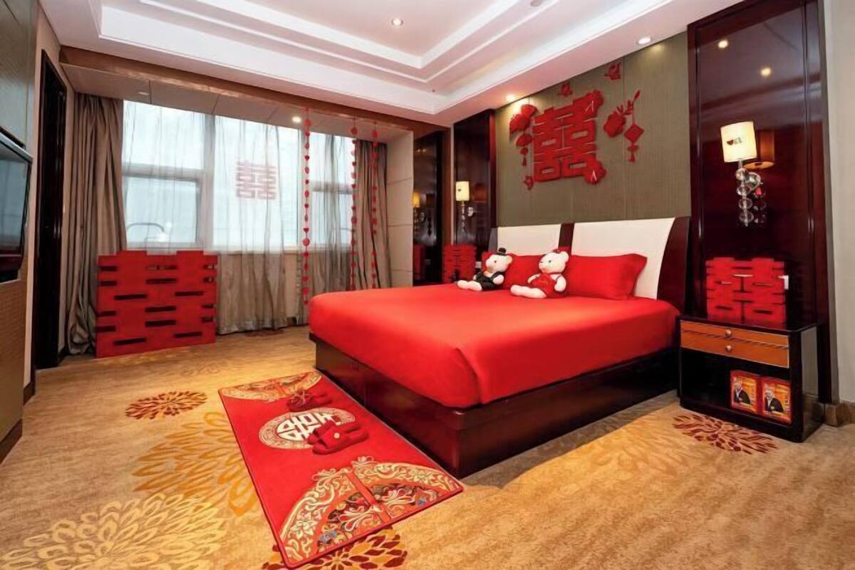 A hotel room with a large bed, a red decorative wall, and a traditional Chinese rug.