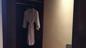 A robe hanging on a rack in a dimly lit room with a plain wall and a door visible. - Zhongwei International Holiday Hotel (Fushun)