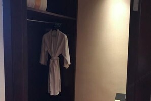 A robe hanging on a rack in a dimly lit room with a plain wall and a door visible. - Zhongwei International Holiday Hotel (Fushun)