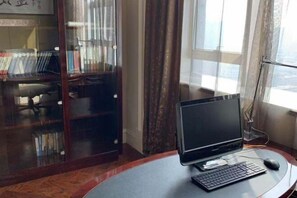 Uma mesa de escritório com monitor, teclado e rato, perto de uma janela com cortinas.