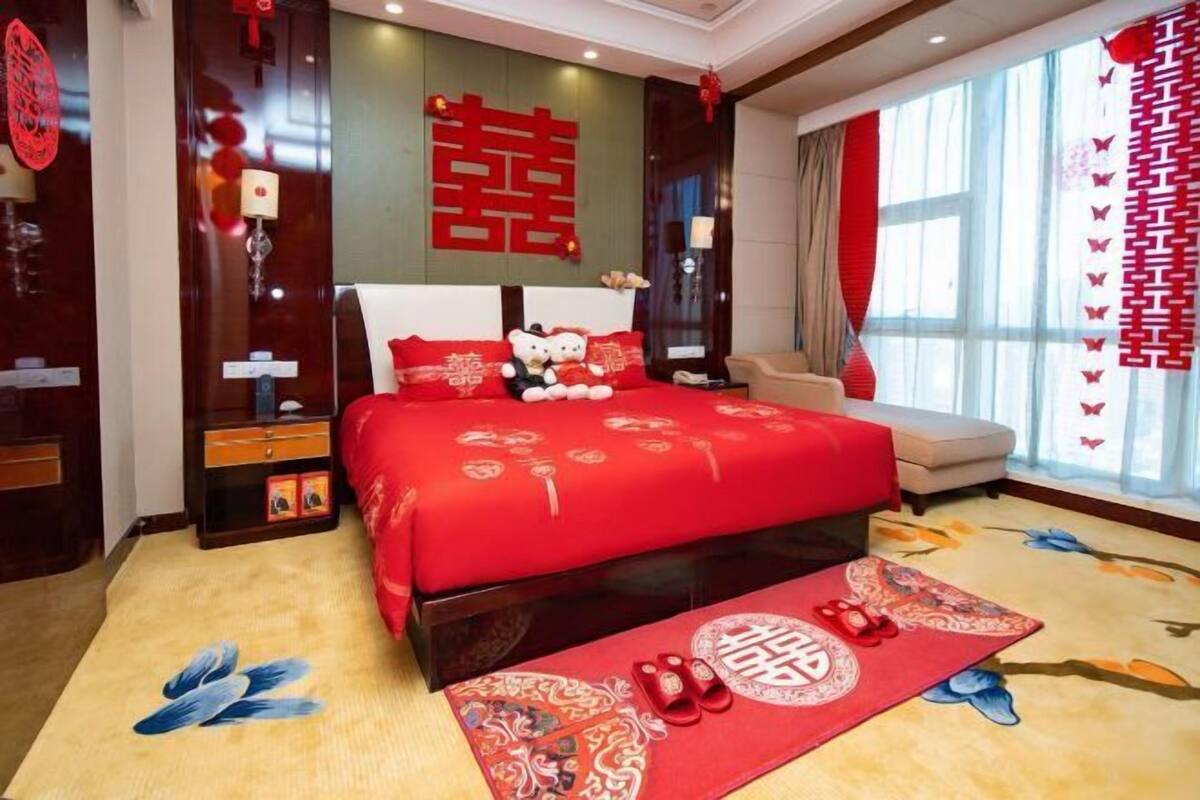 Quarto de hotel com uma cama grande, um sofá, uma mesa de cabeceira e uma janela com cortinas.