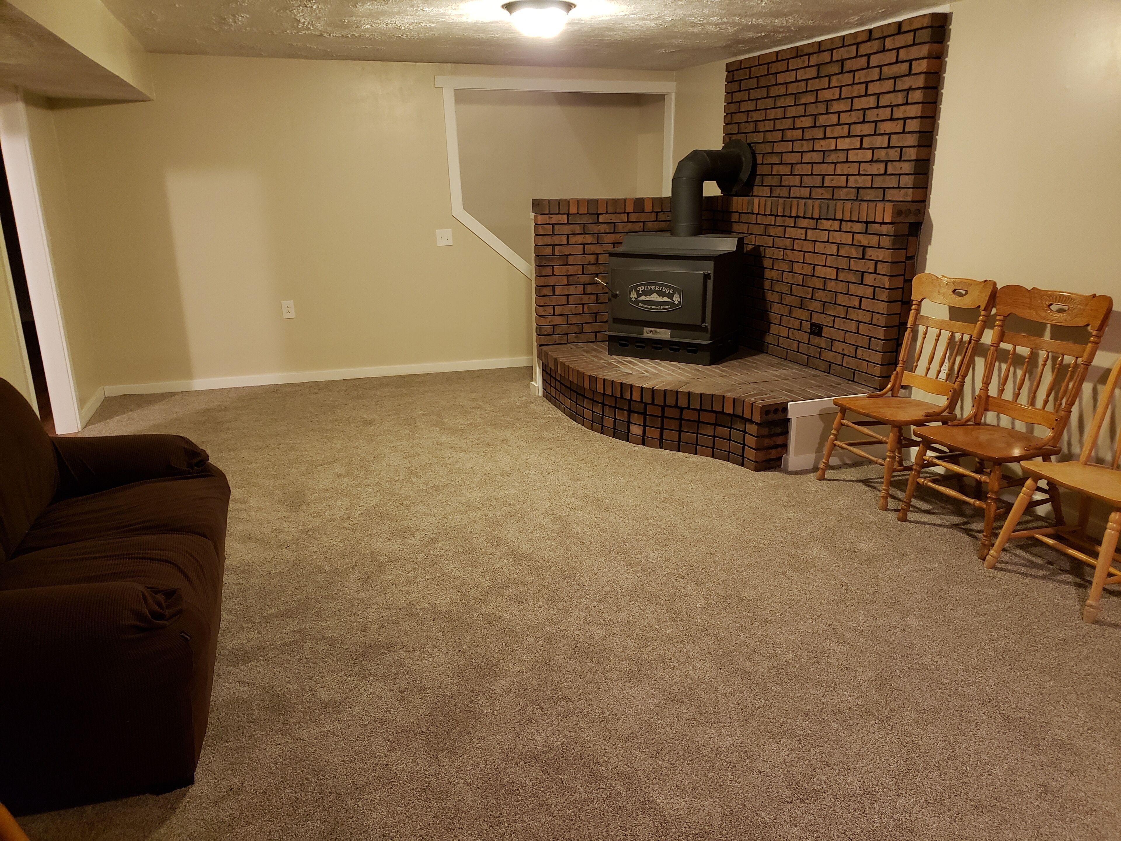A living room with a brick fireplace, a brown sofa, and two wooden chairs.