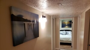 Ein Korridor mit Holzboden, einem Gemälde einer Brücke und einem Bett mit Meerblick.