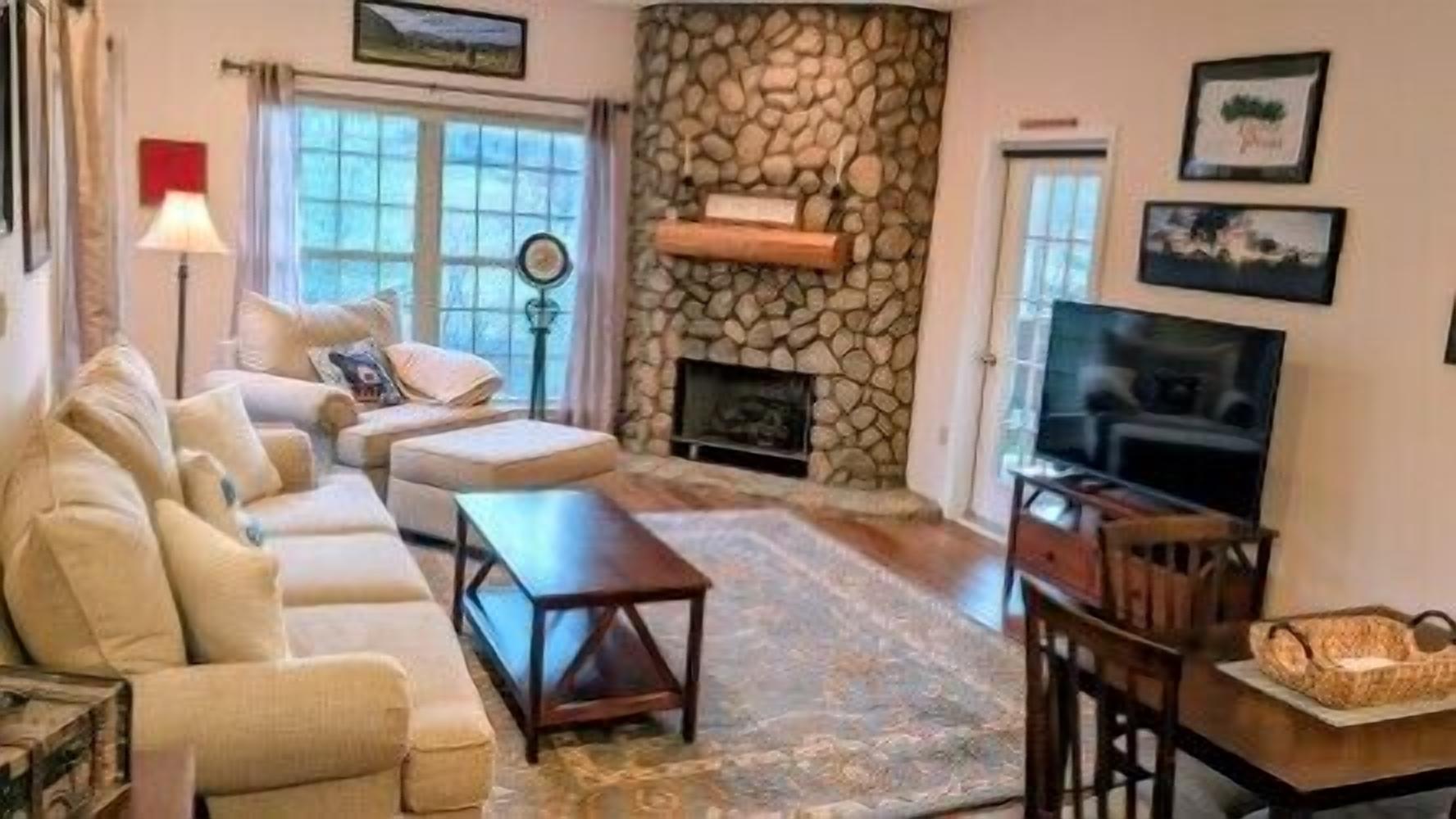 A living room with a sofa, coffee table, fireplace, TV, and stone wall.
