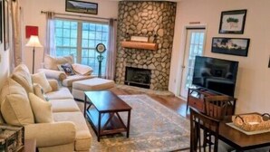 A living room with a sofa, coffee table, fireplace, TV, and stone wall. - Stonecrest 188 at Rumbling Bald (Lake Lure)