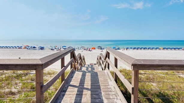 Una passerella di legno che conduce a una spiaggia con ombrelloni e persone.