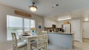 Una cucina con isola centrale, mobili bianchi e un cartello con su scritto 'BEACH HOUSE'.