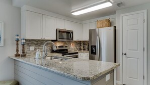 Una cucina moderna con mobili bianchi, un piano di lavoro in granito, elettrodomestici in acciaio inossidabile e un forno a microonde integrato.