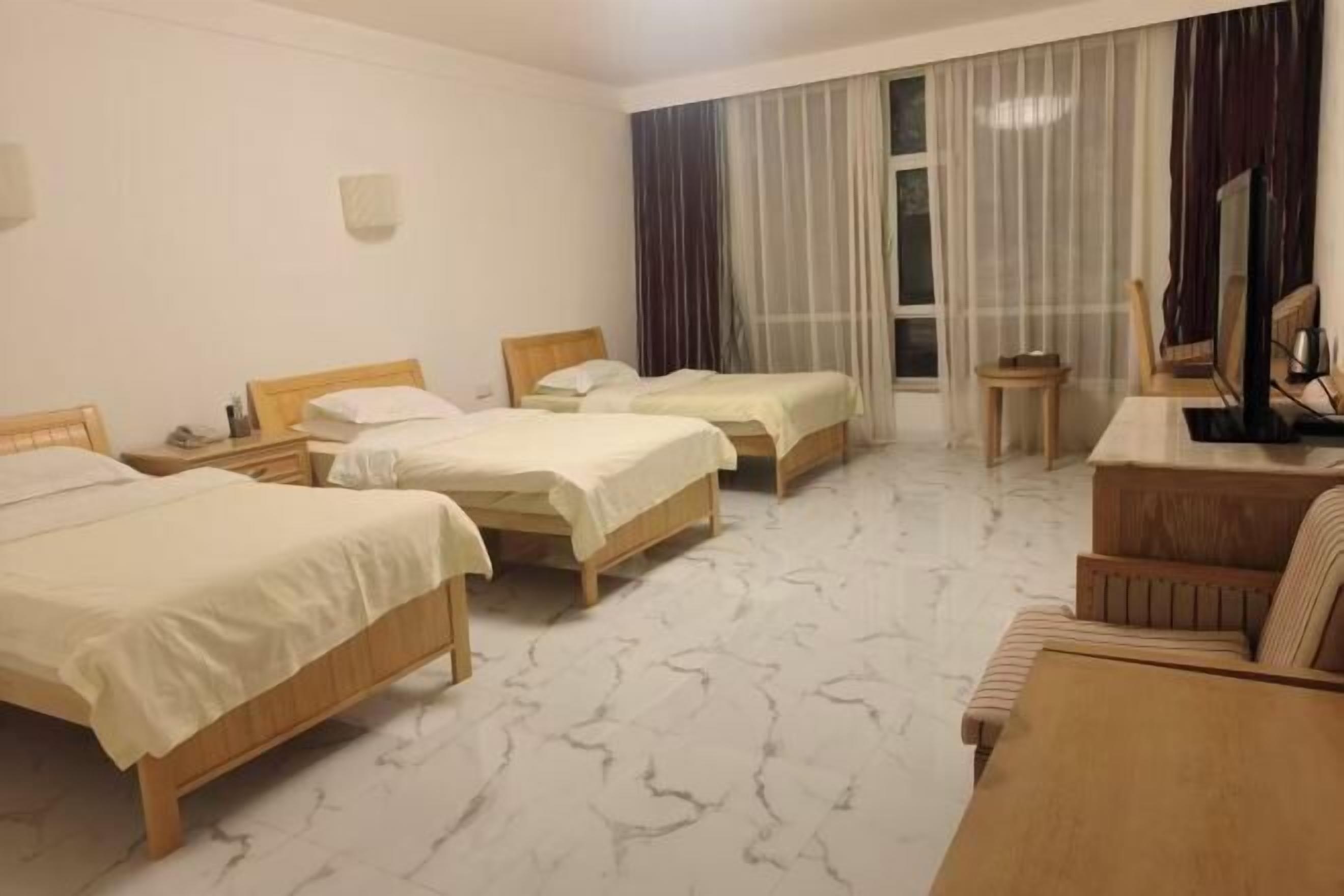 A hotel room with three beds, a wooden desk, a chair, and a large window with curtains.