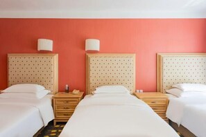 A hotel room with three single beds, wooden headboards, and a red wall.