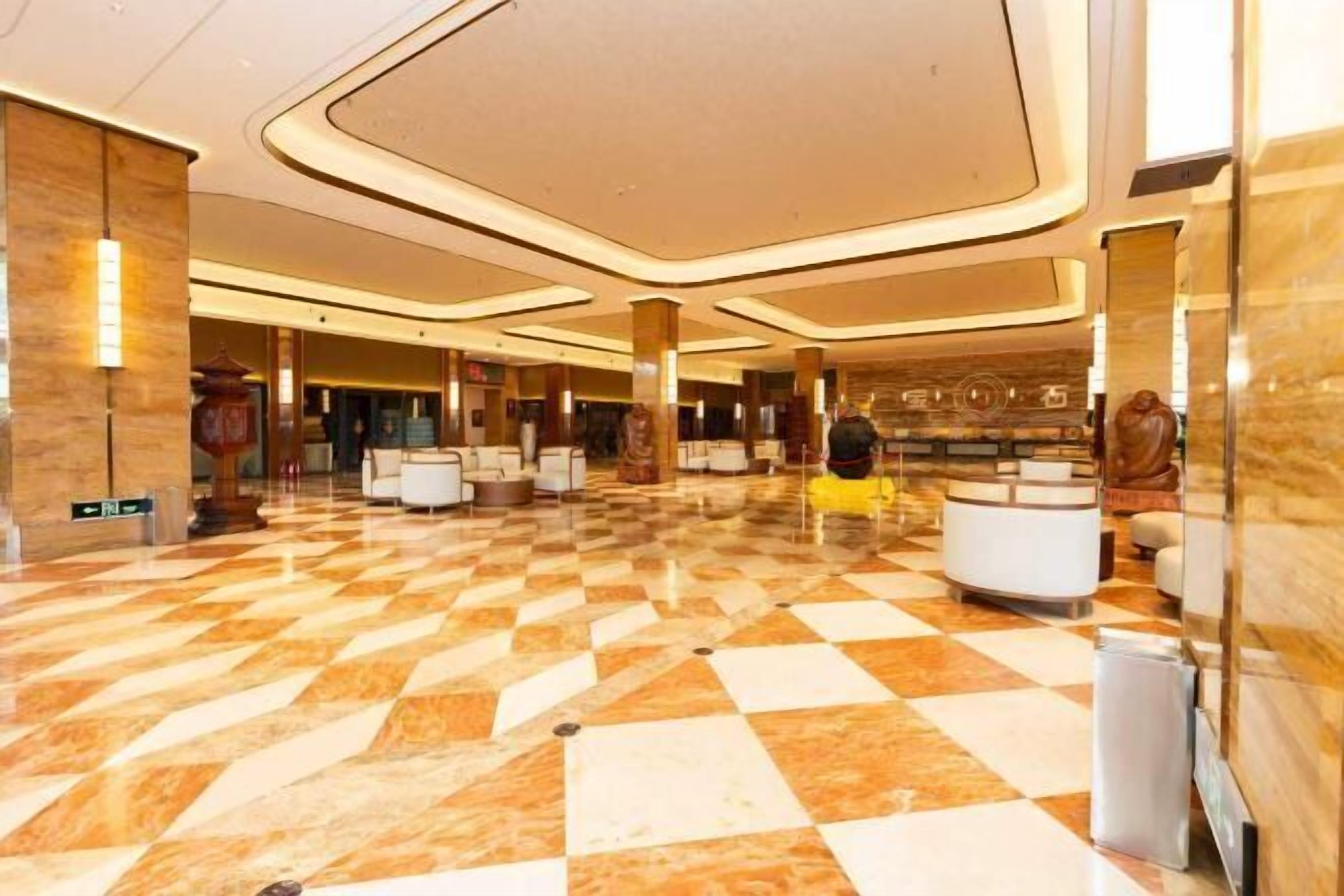 Un hall d’entrée spacieux avec un sol à carreaux, plusieurs espaces aménagés pour s’asseoir et un comptoir d’accueil.
