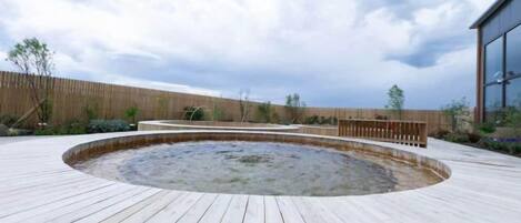 A wooden deck with a hot tub, surrounded by a wooden fence and a building with large windows.