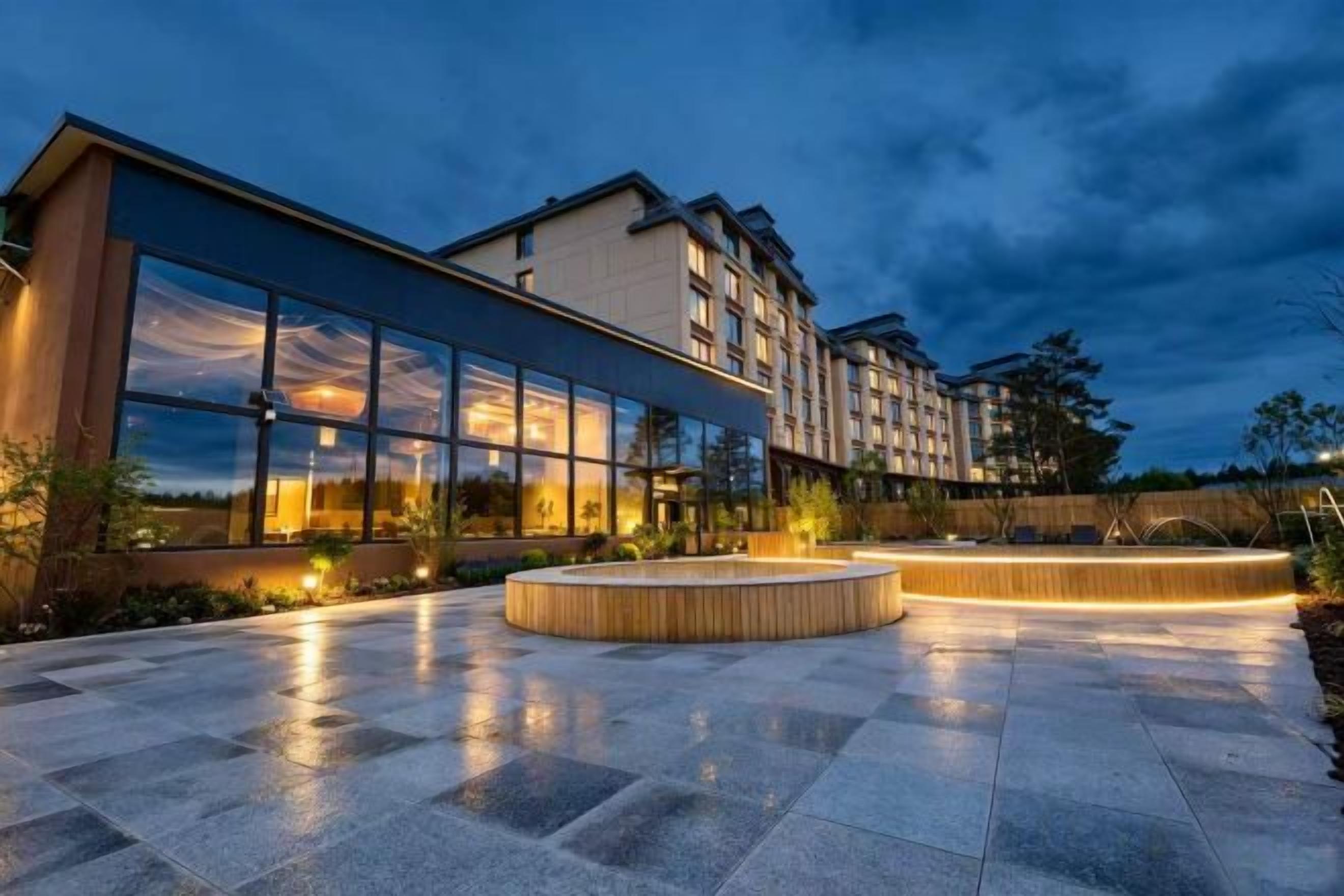 A modern hotel with a spacious outdoor area featuring a circular seating area and a large glass facade.