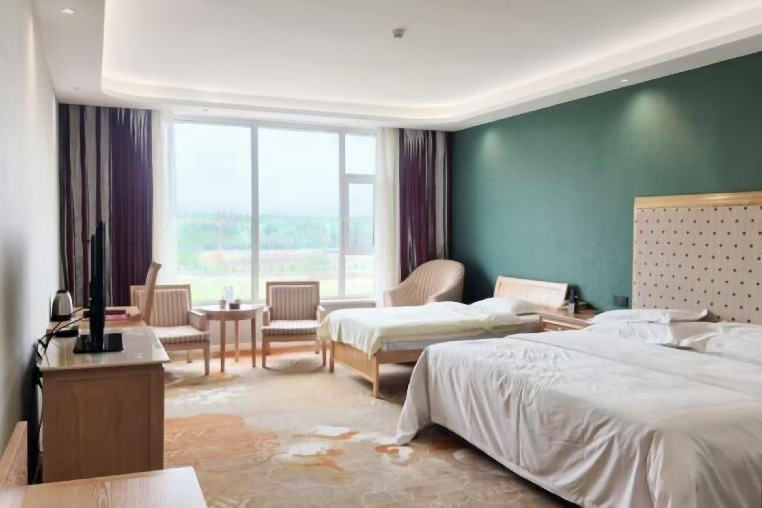 A hotel room with two beds, a desk, a chair, and a view of the outdoors.