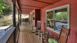 A wooden porch with rocking chairs and a bench, overlooking a forested area.