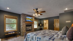 A bedroom with a stone fireplace, a ceiling fan, and a large bed with a checkered bedspread.