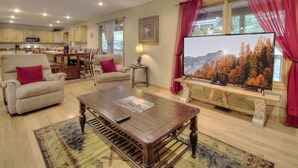 A living room with a wooden coffee table, beige sofas, a TV on a wooden stand, and a kitchen in the background.
