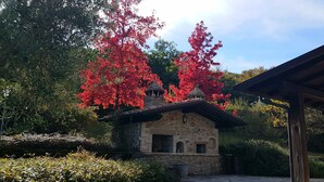 Un edificio de piedra con tejado de baldosas, rodeado de exuberante follaje verde y rojo.
