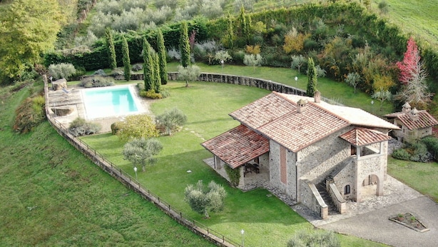 Una villa de piedra con techo de tejas, piscina y un jardín bien cuidado.