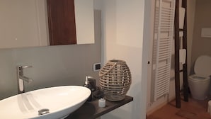 Un baño con lavamanos blanco, espejo, puerta de madera y retrete.