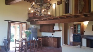 Una cocina amplia con armarios de madera, un comedor con mesa y sillas, una araña y una chimenea.