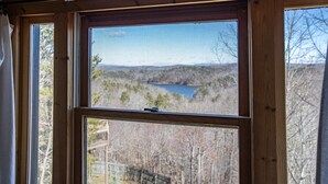 Ein Zimmer mit großem Fenster und Blick auf einen See sowie bewaldete Hügel.