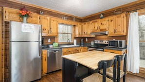 Eine Küche mit Holzausbau, einem Edelstahlkühlschrank, einem Holzessttisch und einem Fenster mit Vorhängen.